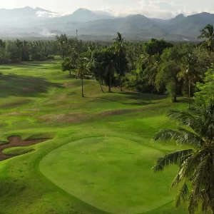 A scenic golf course featuring palm trees with mountains rinjani rising in the background under a clear blue sky.